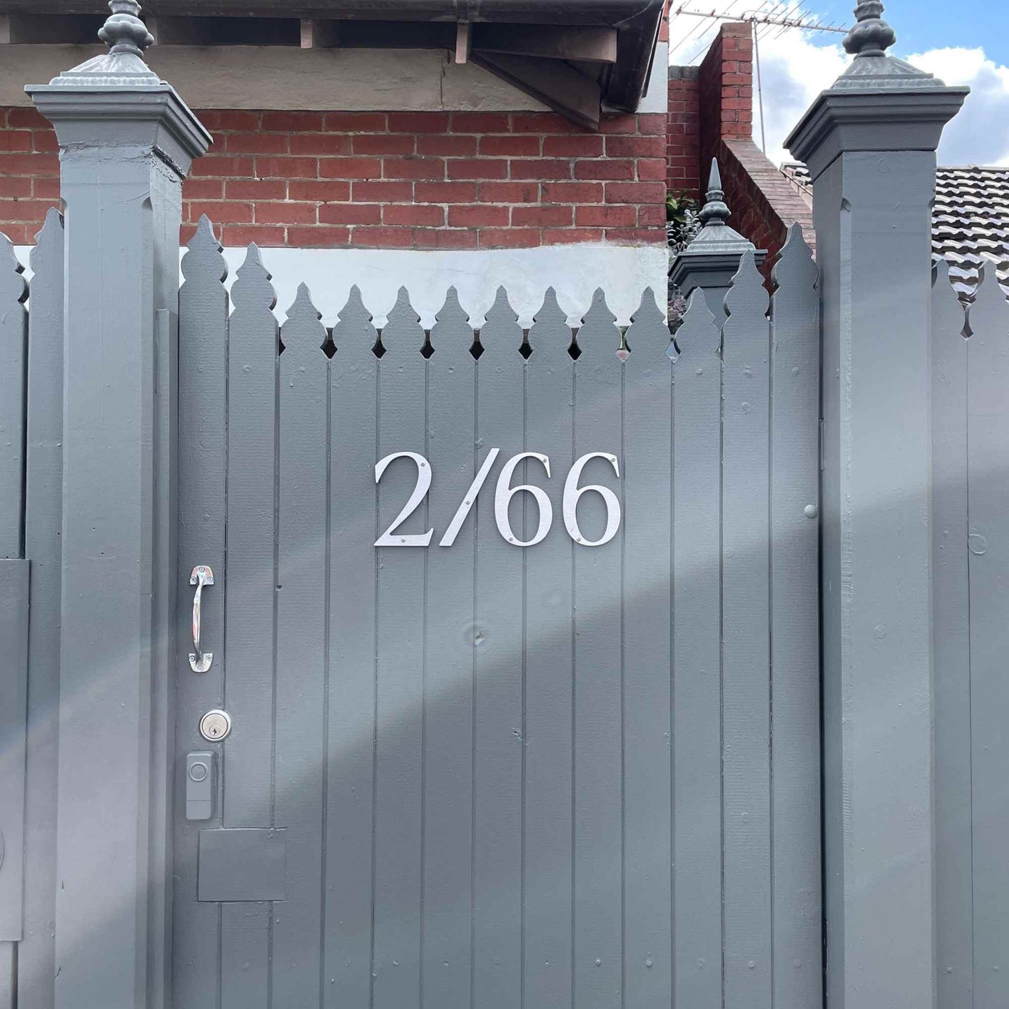 Gray gate with house numbers '2/66' with a brick wall in the background