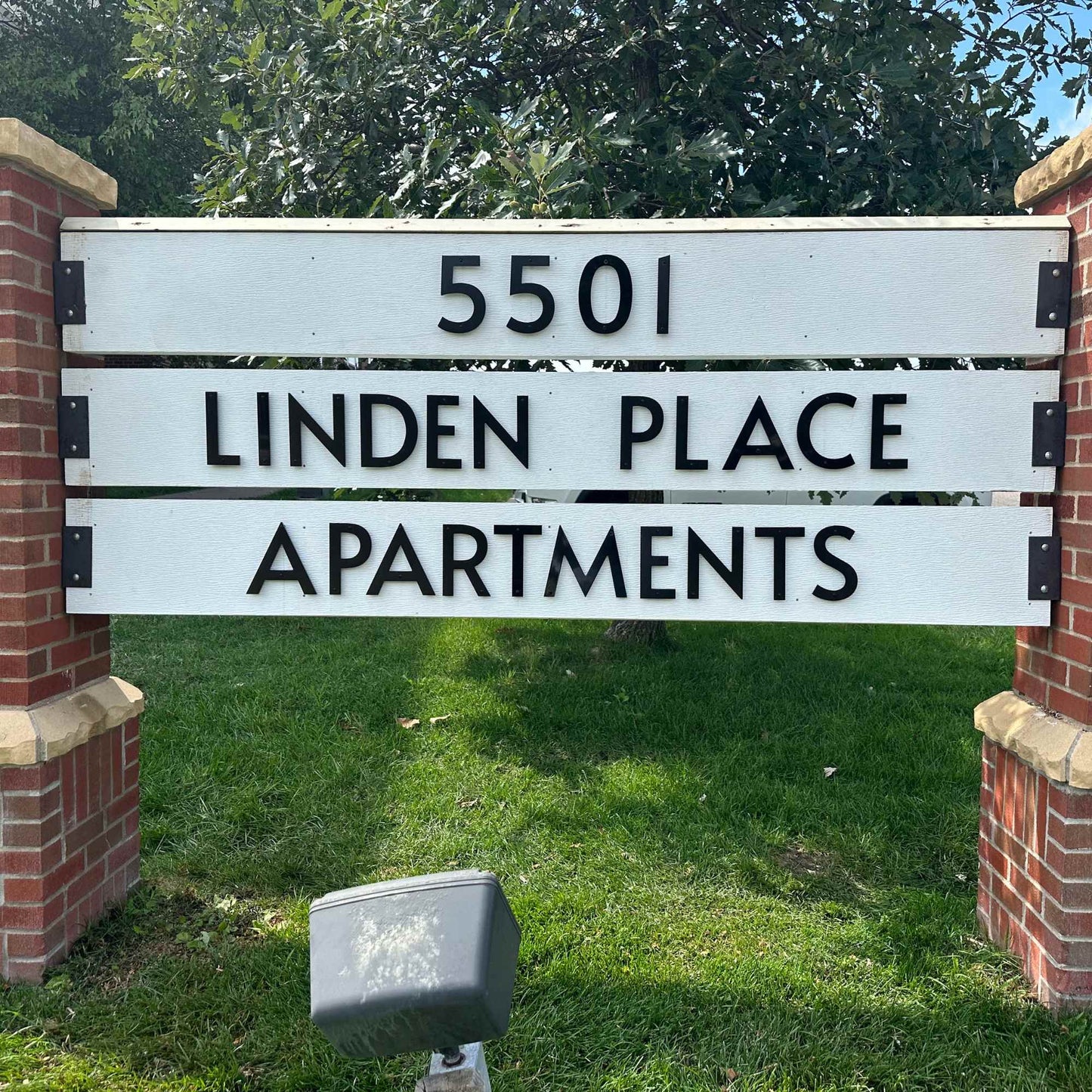 Sign for Linden Place Apartments with address number 5501, surrounded by grass and trees.