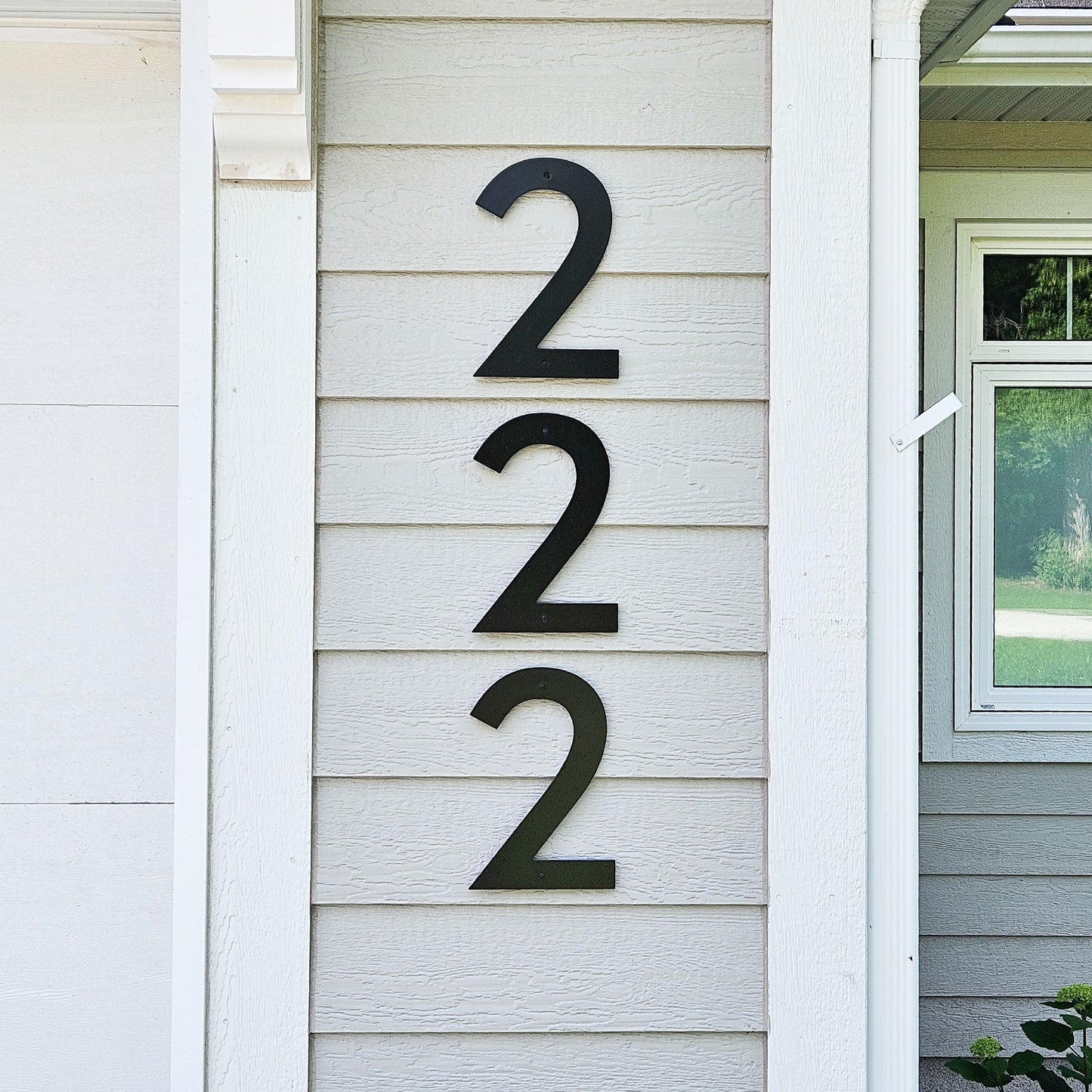 Three large black 12 inch CLASSIC MODERN house numbers reading 222 mounted vertically on a light gray horizontal siding wall next to a white column and window.