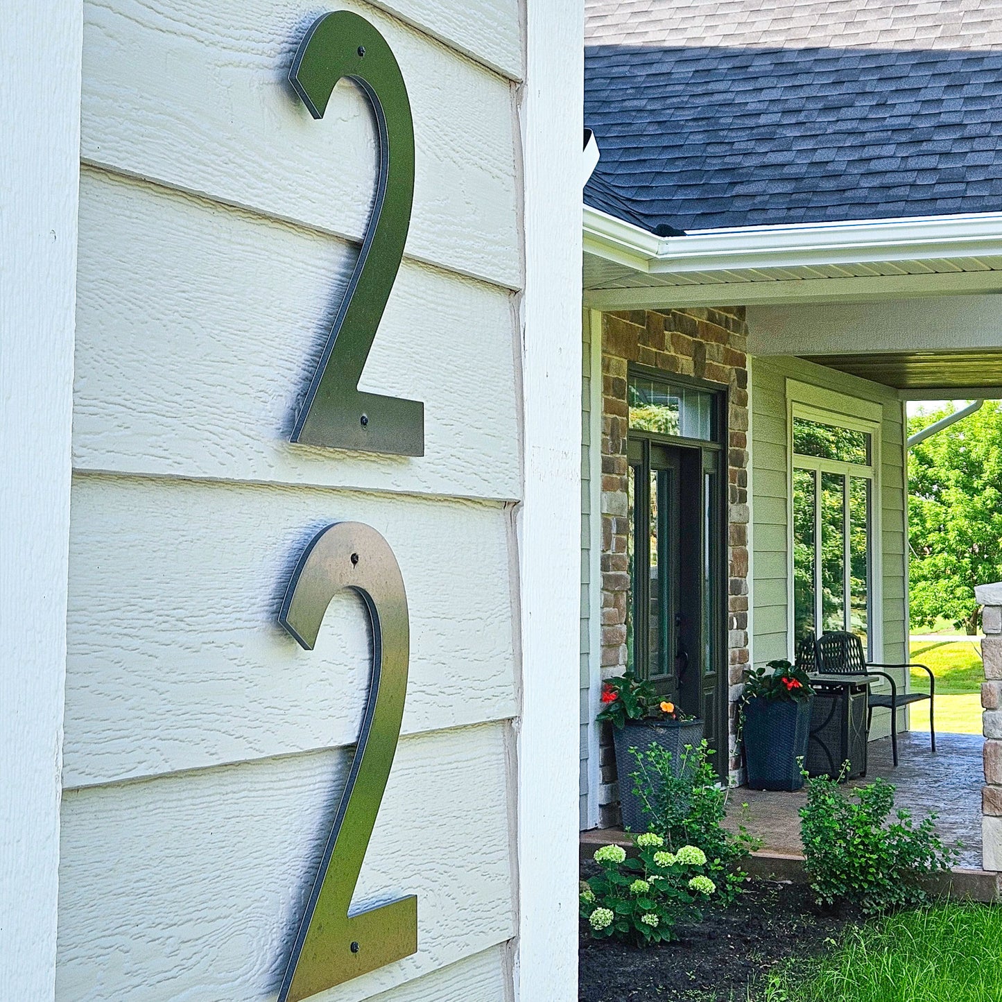 Large 12 inch black CLASSIC MODERN house numbers '22' mounted on white exterior siding next to a porch entryway with brick columns, glass doors, and landscaping.