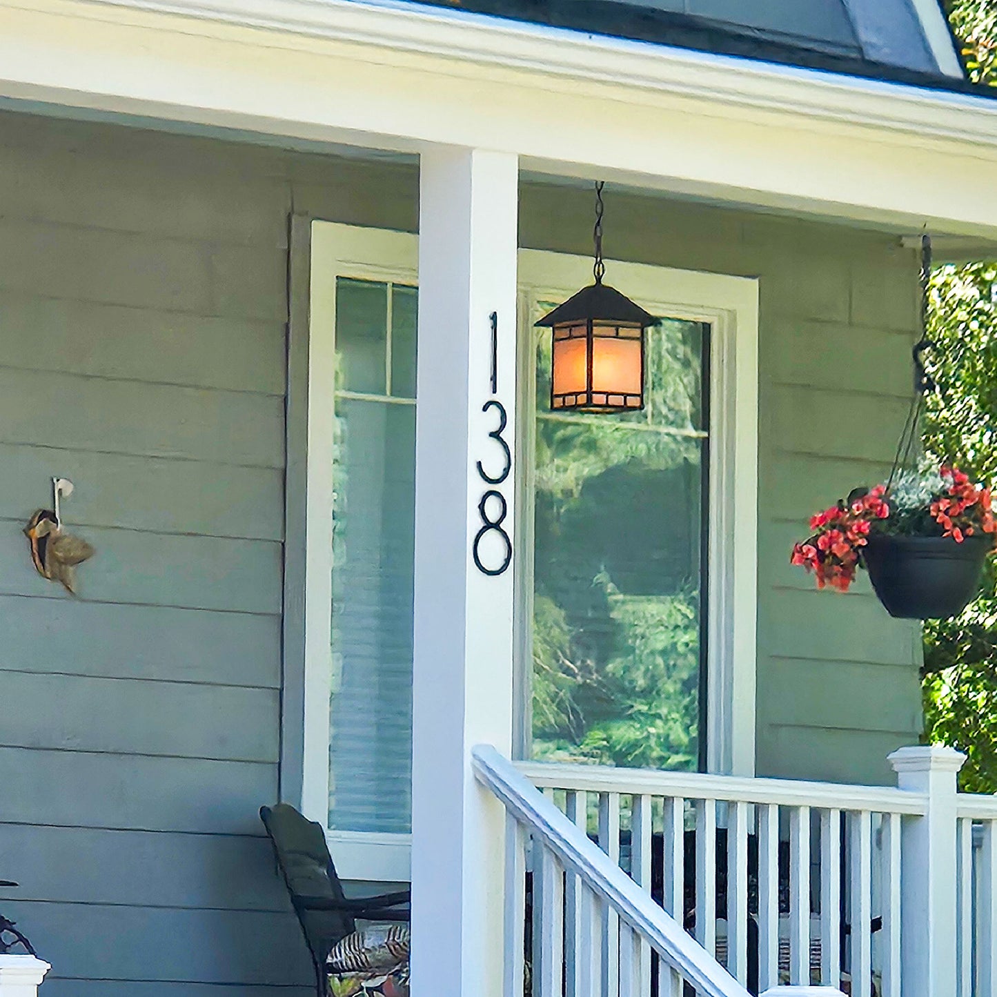 8 inch THIN MDOERN Black plastic house numbers '138' mounted vertically on a white porch post, shown in front of a gray house exterior with a hanging lantern and flower basket.